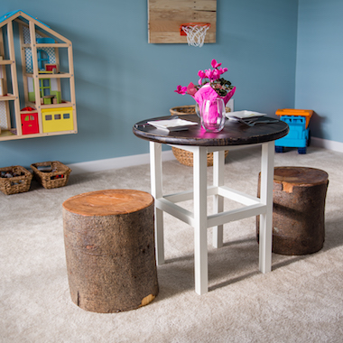 image of a home play area with table, tree stumps for chairs, and a doll house on the wall