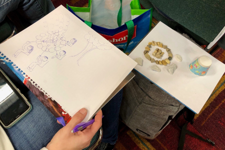 a woman drawing a sketch of children around a campfire on her lap