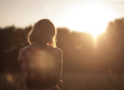 a peaceful woman sitting in front of trees at sunset